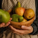 Cozy scene of a person holding a wooden bowl filled with pears and apples.