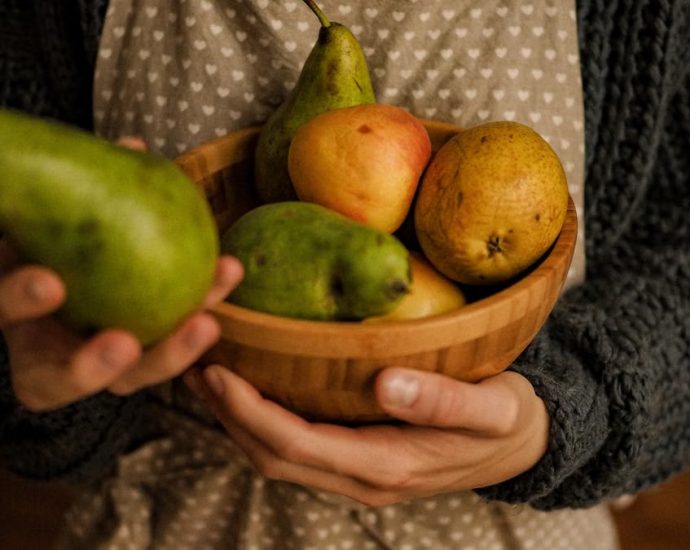 Cozy scene of a person holding a wooden bowl filled with pears and apples.