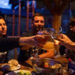 Friends clinking glasses at an outdoor dinner party, enjoying food and drinks.