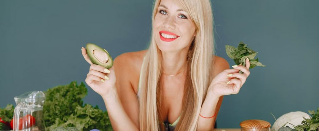 Blonde woman promotes healthy eating with fresh vegetables and fruits on display.
