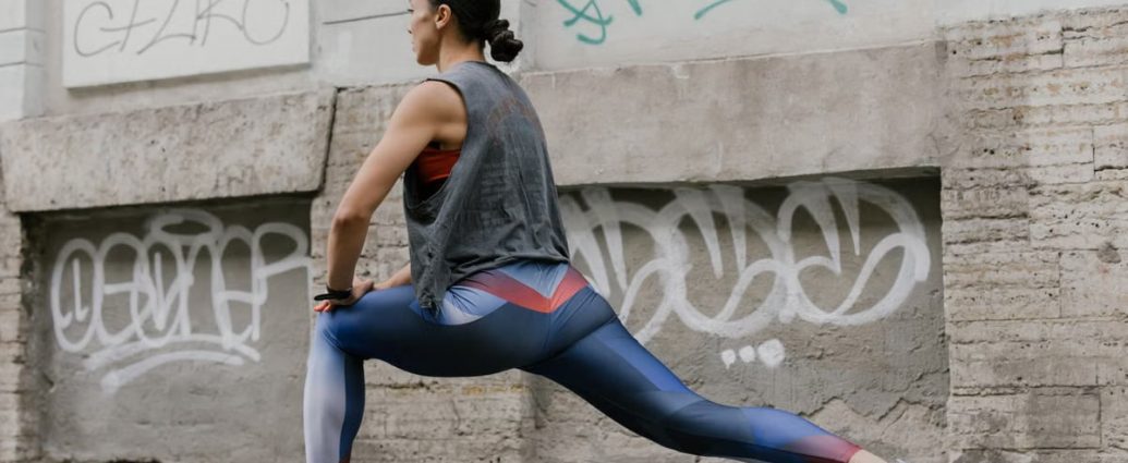 Woman doing lunges for fitness against an urban graffiti wall, showcasing exercise and wellness.